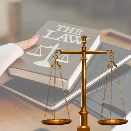 Pago de abogados de lesiones personales en Nueva York. Detrás, una abogada con un libro de leyes. Delante, una balanza en cobre.