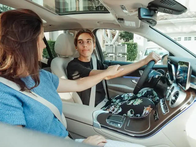 A parent teaching a teen driver safety skills in a car, focusing on handling back-to-school road hazards in August.