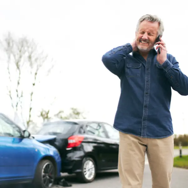 Person standing next to a damaged car while making an emergency call, appearing to be injured and seeking help