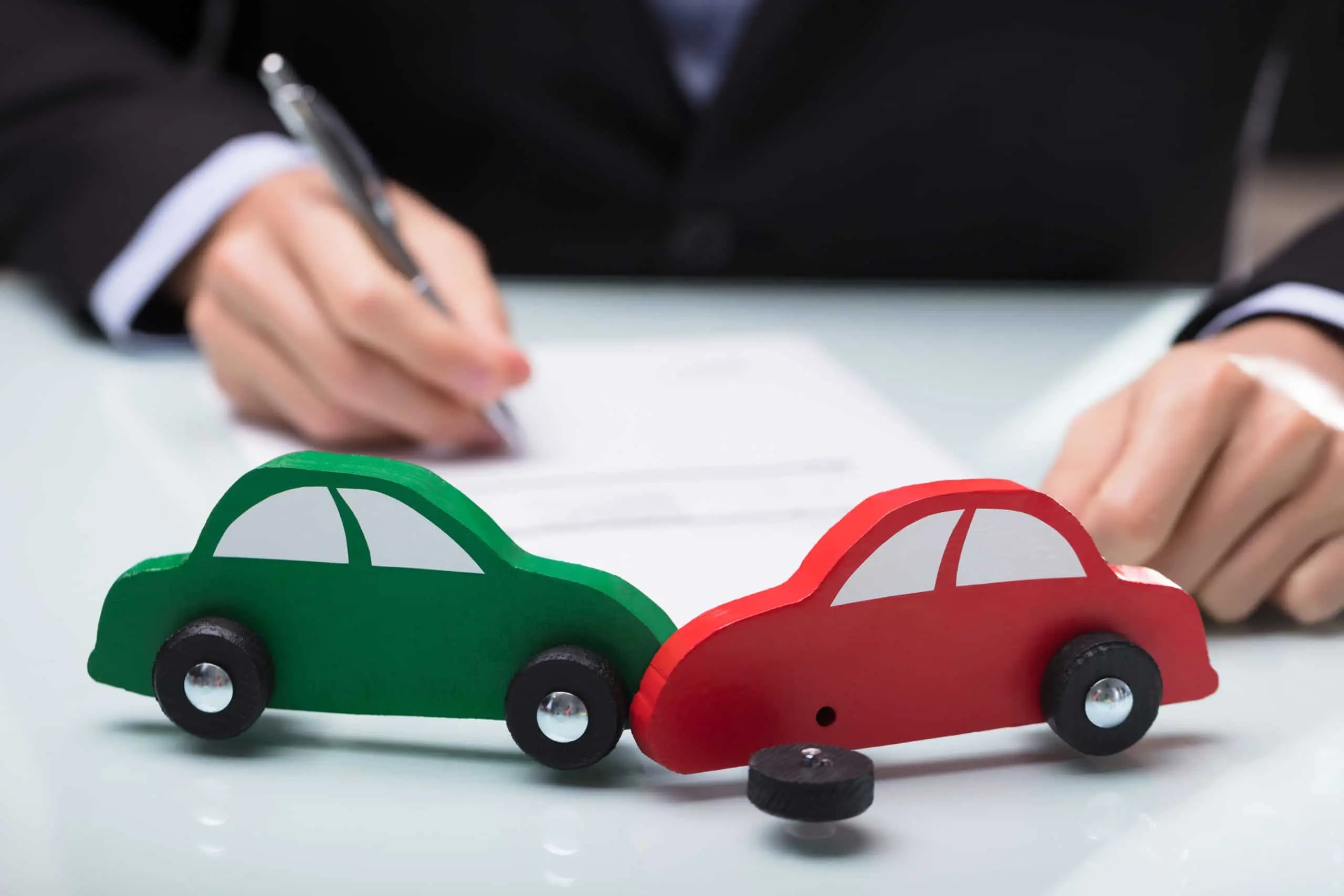 Close-up Of Red And Green Car In Front Of Businessman Writing On Paper