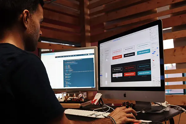 person viewing two computer monitors working on web design