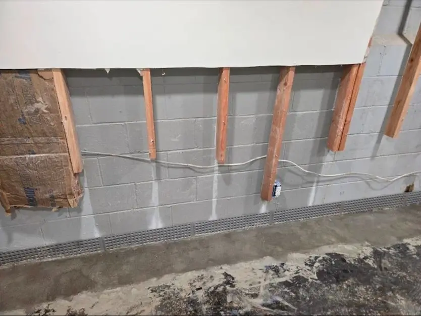 Basement wall with exposed framing and drainage system, highlighting moisture management for NJ waterproofing solutions.