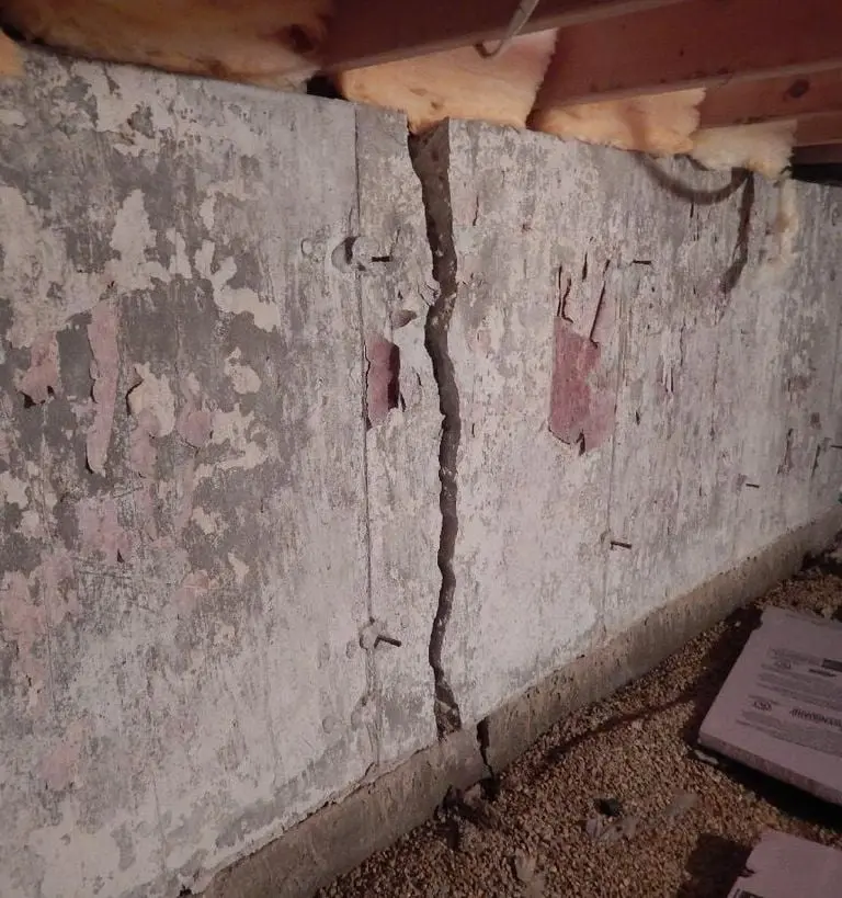 Cracked basement wall showing peeling paint and exposed concrete, highlighting foundation damage relevant to basement repair and waterproofing services.