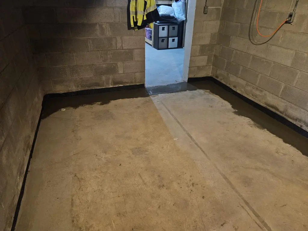 Interior basement with newly installed drain tile system along the perimeter, showcasing concrete floor and cinder block walls, emphasizing waterproofing solutions for storm protection.
