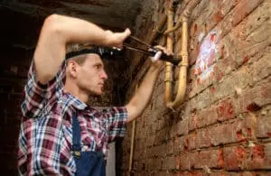 Man using a wrench to repair plumbing pipes on a brick wall in a basement setting, illustrating basement waterproofing and repair services.