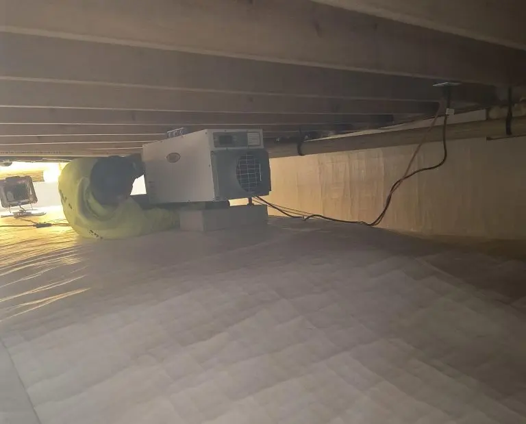 Technician installing Aprilaire dehumidifier in crawl space to control humidity and prevent moisture-related damage.