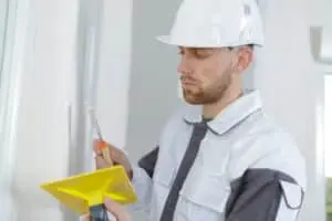 Construction worker in hard hat using a trowel and yellow scoop for foundation repair tasks.