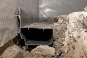 Basement drainage system installation with a plastic drain channel surrounded by gravel and soil, emphasizing effective waterproofing solutions for structural integrity.