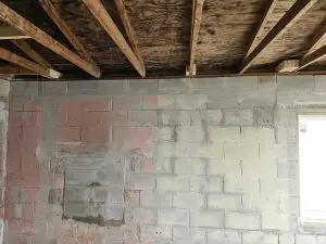 Concrete block basement foundation wall with patched masonry, visible cracking, and exposed wooden floor joists before bowed wall repair.