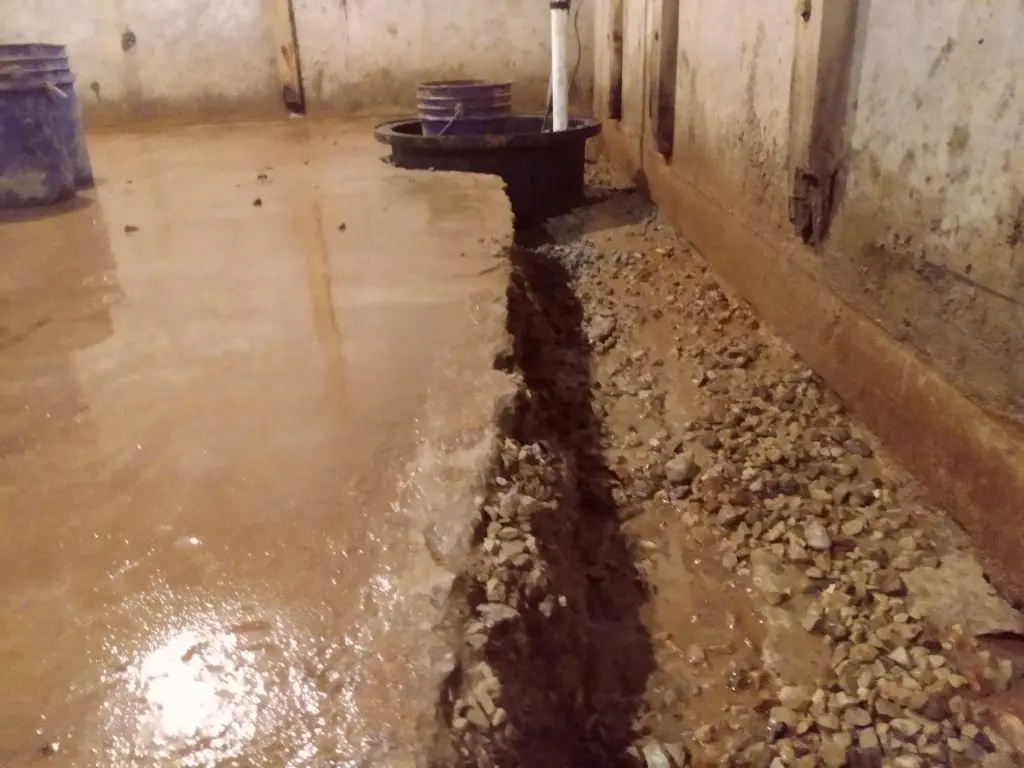 Interior basement showing water control measures with gravel drainage, concrete floor, and water pooling, emphasizing waterproofing importance for preventing water damage and enhancing property value.
