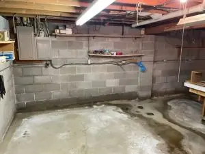 Unfinished basement with concrete block walls, visible floor moisture, and water stains illustrating basement waterproofing concerns in Milwaukee.