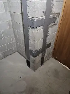 Corner of a basement wall featuring concrete blocks with metal reinforcement, illustrating foundation repair techniques and structural stability.