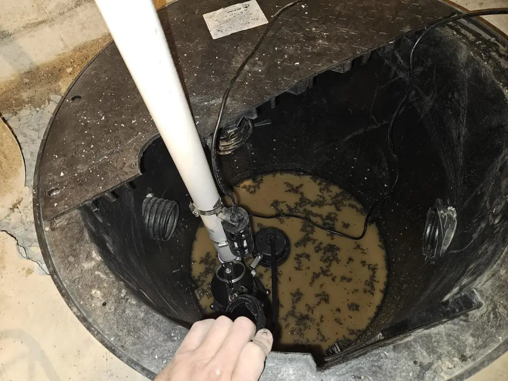 Sump pump installation in a basement, showcasing water accumulation and plumbing components, relevant to basement waterproofing and repair services.