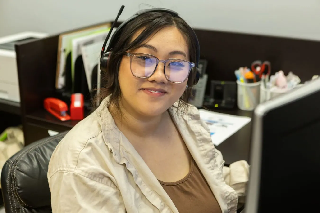 Young woman with headset smiling at computer in office, representing customer service role at Basement Repair Specialists, emphasizing teamwork and employee engagement.