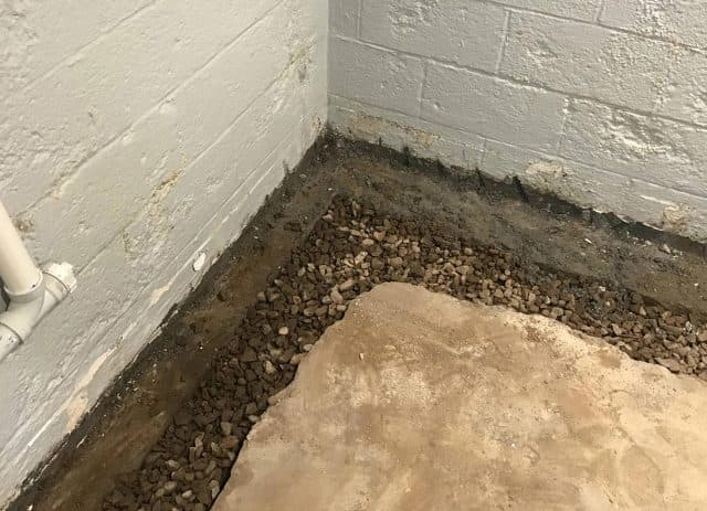 Corner of a basement showing gravel and stone foundation for effective drainage, highlighting French drain installation for water management.