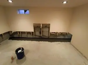 Basement with exposed lower walls revealing insulation and wooden studs. Bare concrete floor, bucket, and bottle in the foreground, unfinished appearance.