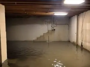 Flooded basement with standing water, visible concrete walls, and stairs, illustrating the effects of seasonal water intrusion and the need for effective waterproofing solutions.