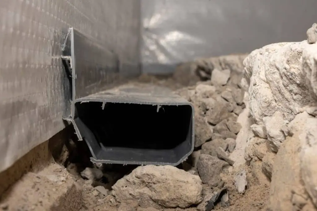 Drain tile system installed in a basement, surrounded by gravel and soil, illustrating basement waterproofing solutions to prevent water damage.