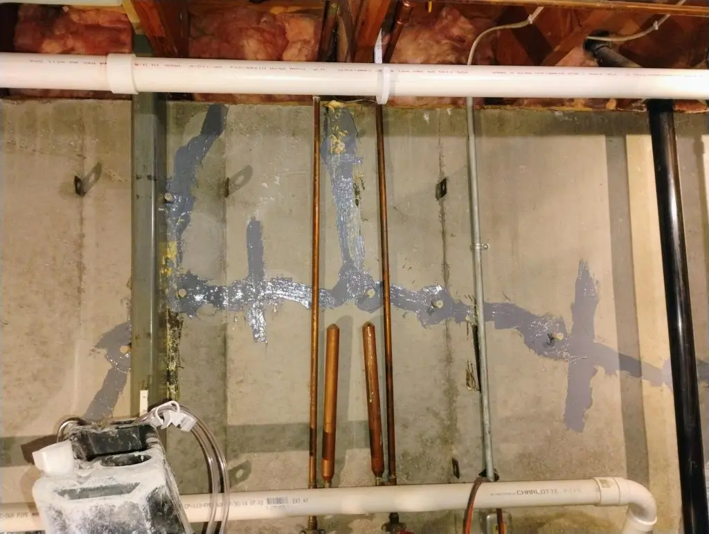 Basement wall with visible crack repairs, including gray sealant, pipes, and insulation, illustrating the importance of foundation maintenance and inspection for home safety.