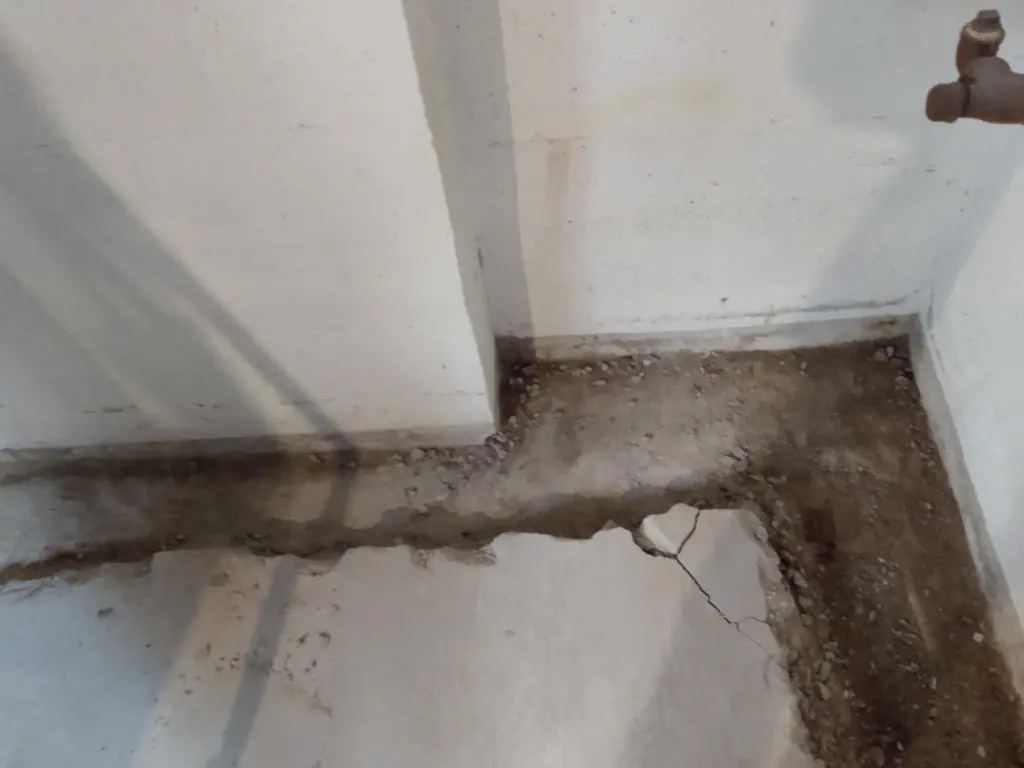 Interior basement corner showing cracked concrete floor and exposed dirt, indicating potential water damage risks, relevant for fall maintenance checklist.