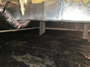 Crawl space with black vapor barrier on the ground, exposed insulation and ductwork on the ceiling, and concrete block walls. Dimly lit, utilitarian atmosphere.