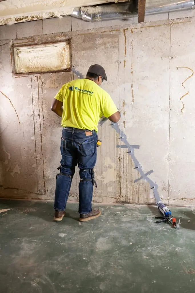 Worker applying crack repair sealant on a basement wall, emphasizing waterproofing techniques for home maintenance.