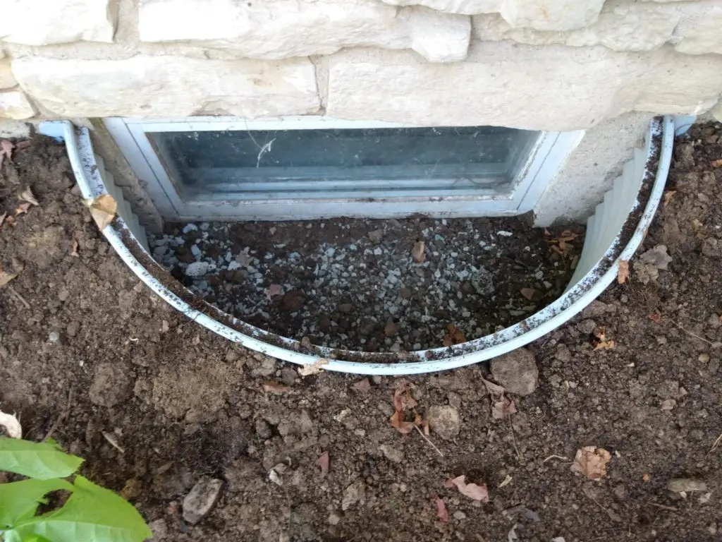 Window well installation with gravel and soil surrounding a basement window, highlighting potential moisture management solutions for basement repair.