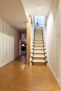 Stairway to finished basement in home interior with wood paneling and cork flooring.