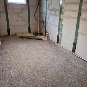 Interior basement space with exposed walls, gray flooring, and sump pump setup, illustrating effective drainage solutions for preventing water infiltration and flooding.
