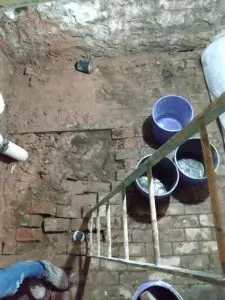 Basement floor with exposed bricks, water pooling in buckets, and a ladder, illustrating potential sources of basement leaks and water damage.