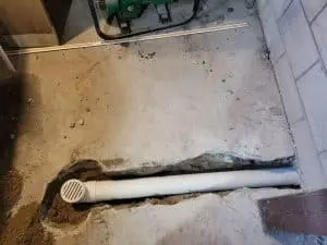 Interior basement floor drain installation with a white drainage pipe and surrounding concrete, illustrating effective water management solutions for preventing basement water issues.