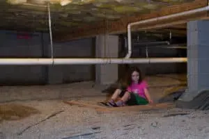 young girl sitting under home in crawlspace