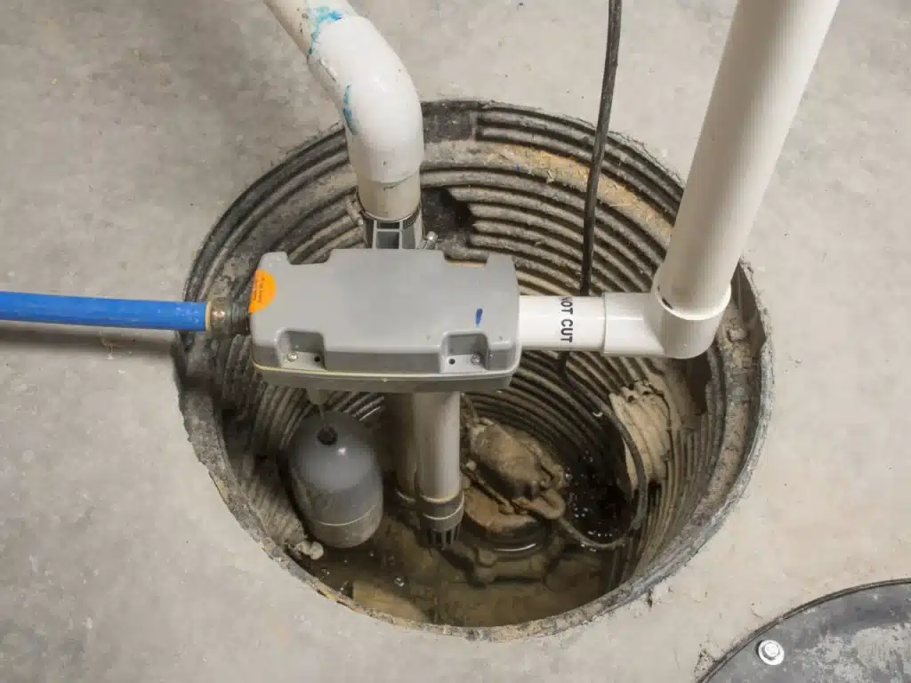 Sump pump system installed in a basement, featuring a gray pump unit, blue discharge hose, and PVC piping, illustrating waterproofing solutions for basement water damage prevention.