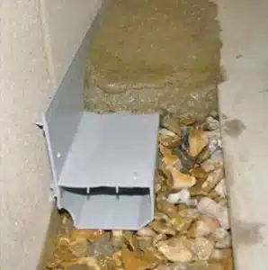 Interior French drain system with gravel and water flow, illustrating effective basement waterproofing solutions.