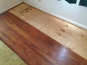 Sagging floor repair in Indianapolis showing repaired wood subfloor beside existing hardwood flooring