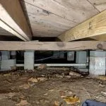 Crawl space with exposed wooden joists and support piers showing structural sagging and uneven support