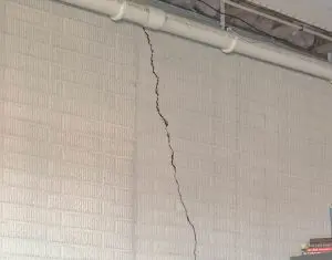 Vertical crack in concrete wall, indicating potential foundation settling issues, with visible texture and a nearby stack of books.