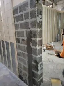 Foundation wall with visible repair work, showcasing carbon fiber reinforcement application and masonry texture, in a construction setting related to foundation stability and repair methods.