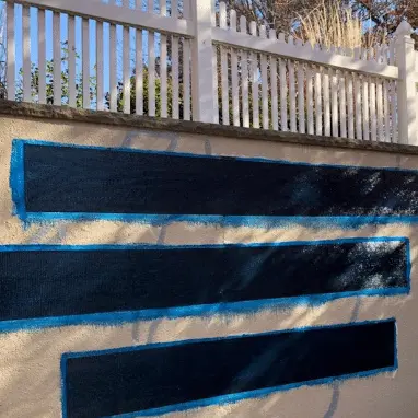 Wall with blue-painted horizontal strips, illustrating foundation repair preparation, surrounded by a white fence, highlighting StablWall's structural strengthening solutions.