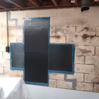 Carbon fiber reinforcement system applied to a basement wall, showcasing structural repair for foundation stability, with visible blue outlines and a concrete block background.