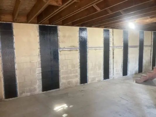 Interior view of a basement wall with applied carbon fiber strips for foundation reinforcement, showcasing the preparation for StablWall's structural strengthening system.