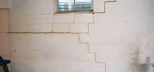 Basement wall with visible cracks near a window, illustrating potential damage caused by tree roots and soil issues, relevant to foundation repair discussions.