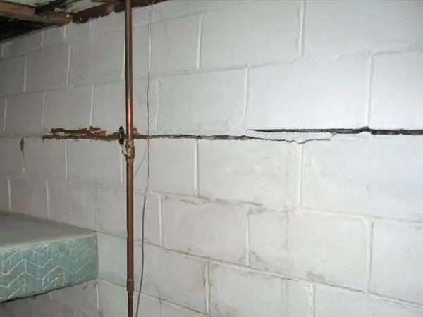 Bowed basement wall with visible cracks and plumbing pipe, illustrating foundation damage requiring repair solutions.