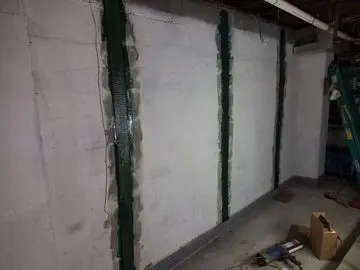 Carbon fiber reinforcement applied to a basement wall, showcasing structural support methods for foundation repair, with tools and materials visible on the floor.
