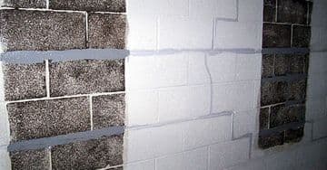 Bowed basement wall with visible cracks and carbon fiber reinforcement strips applied for foundation repair.