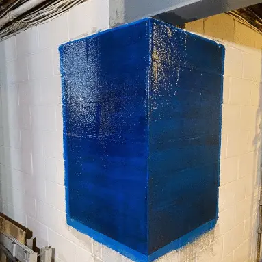 Corner of a foundation wall painted blue, showcasing structural reinforcement application in a basement setting, illustrating StablWall's carbon-fiber system for foundation stabilization.