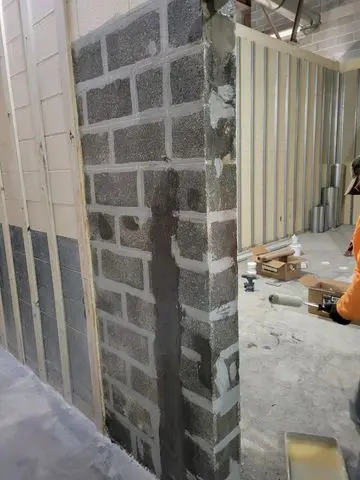Foundation wall with visible repair work, showcasing carbon fiber reinforcement application and masonry texture, in a construction setting related to foundation stability and repair methods.