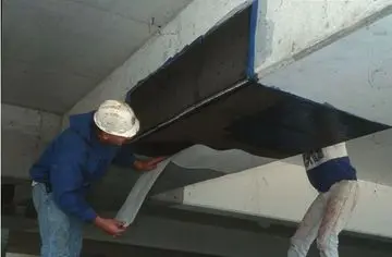 Workers applying carbon fiber reinforcement to a concrete beam, showcasing advanced foundation repair technology for enhanced structural integrity.