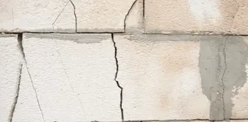 Cracked foundation wall showing visible stair step cracks and varying surface textures, illustrating potential structural issues related to foundation stability.
