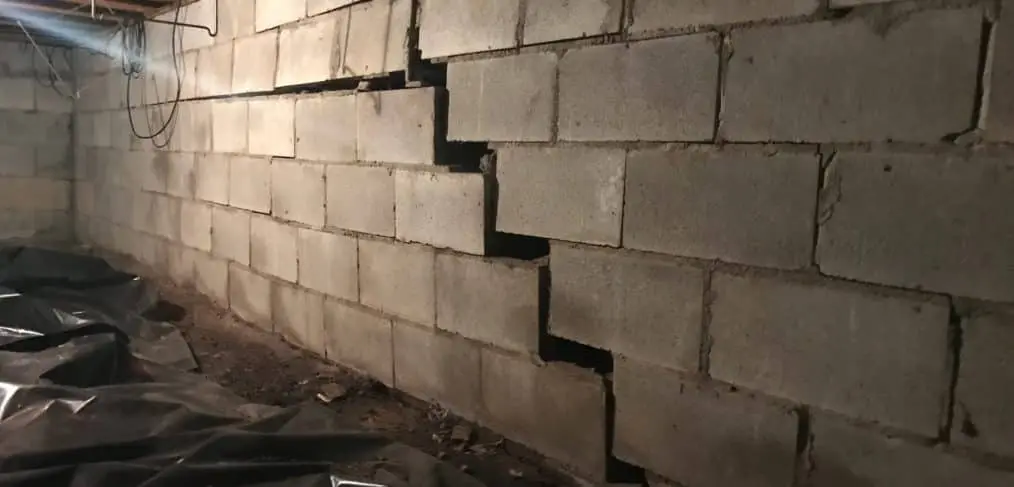 Basement wall with visible cracks in concrete blocks, illustrating structural damage and the need for carbon fiber wall repair and reinforcement solutions.